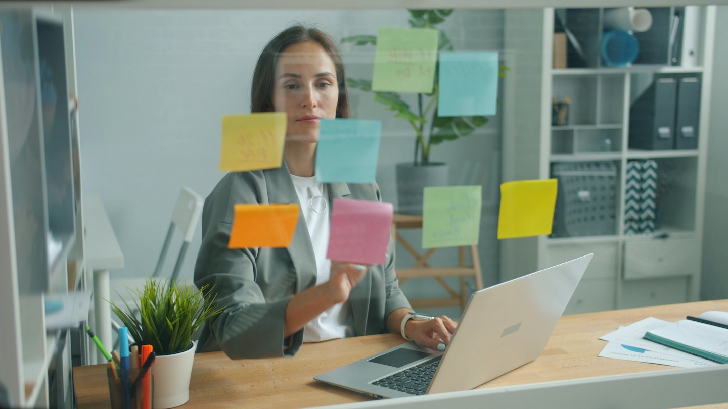 Donna organizza post-it colorati su una parete divisoria in vetro dell'ufficio.